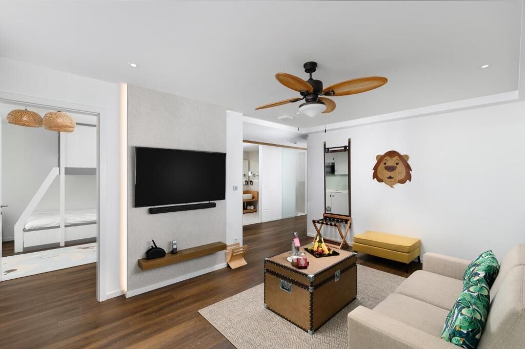 A modern living room with a flat-screen TV, a ceiling fan, a sofa, a coffee table, and a small bench.