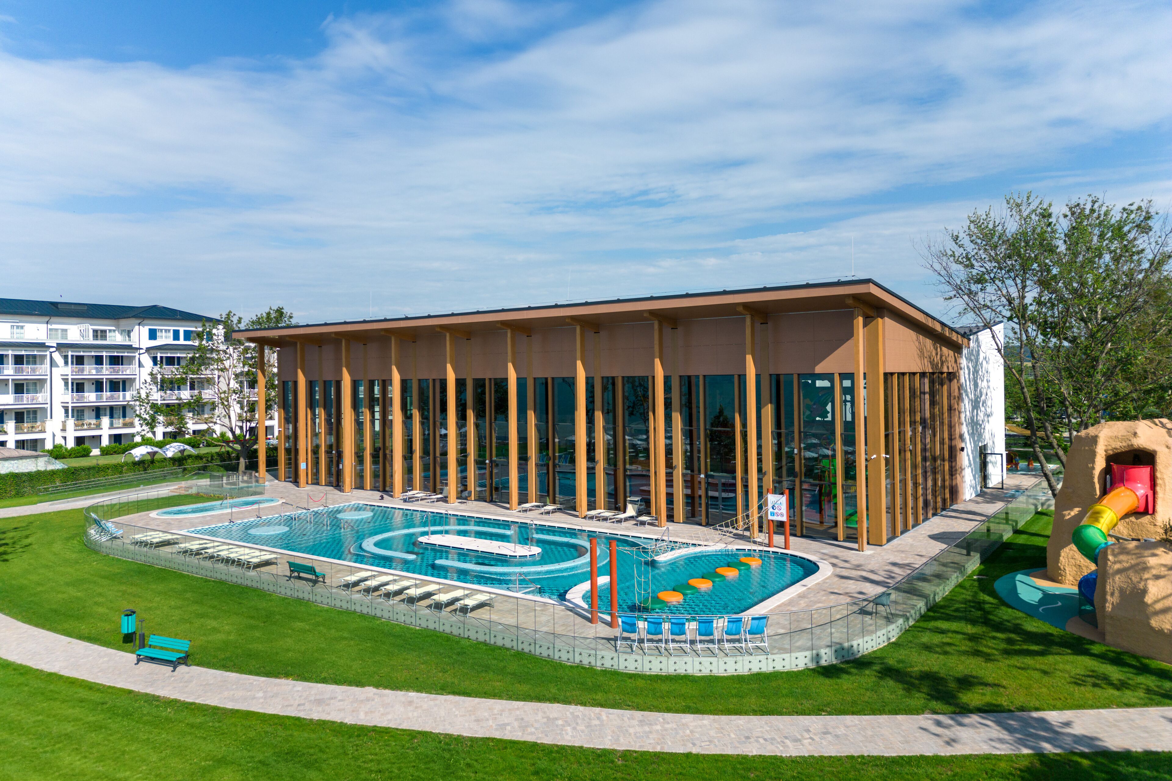 A modern hotel with a large swimming pool, outdoor seating, and a children's play area.