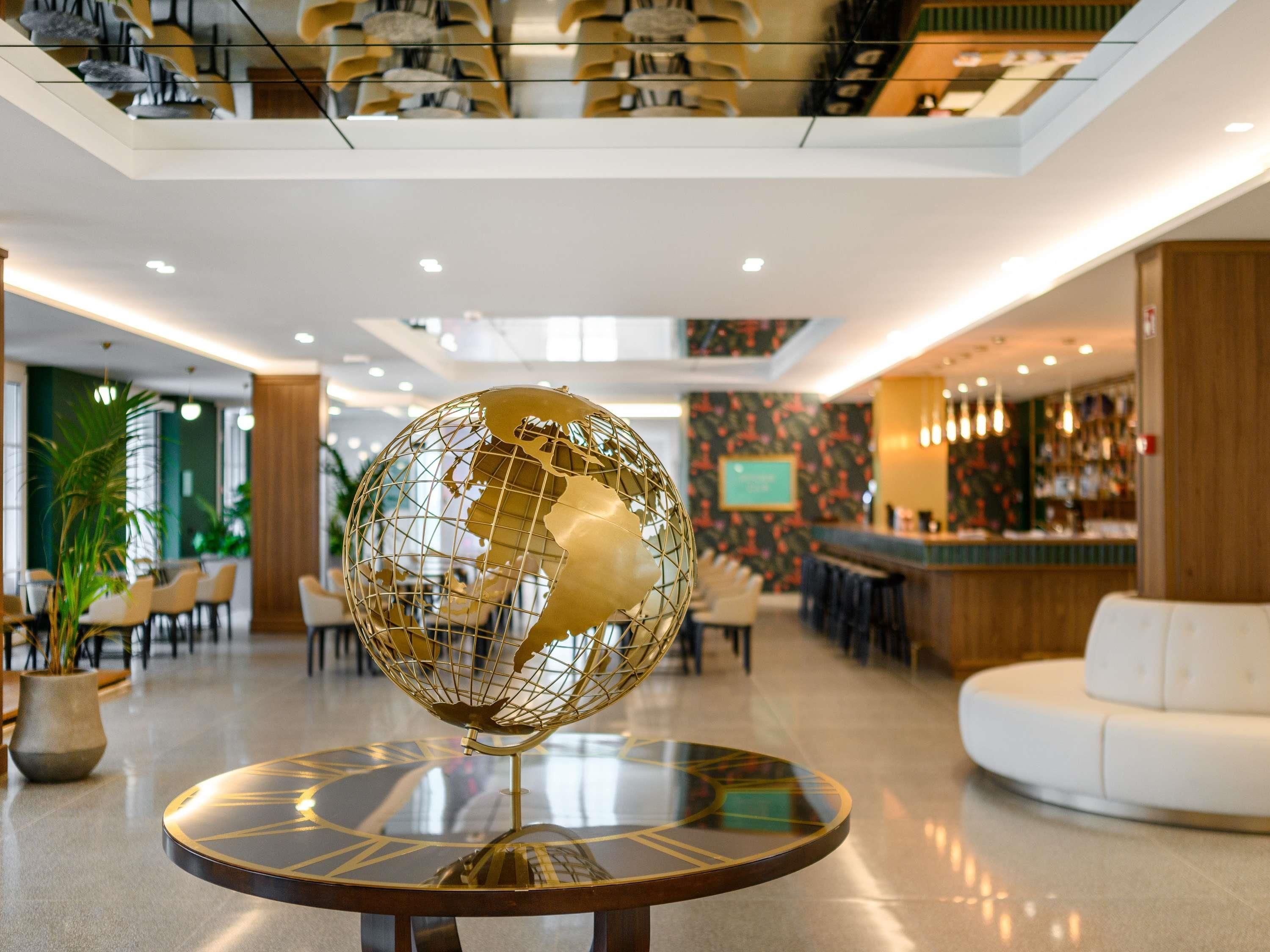 A lobby with a round table featuring a golden globe, a white sofa, and a bar area in the background.