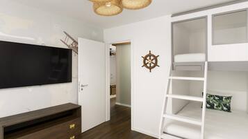 Quarto com cama de solteiro, televisão, cómoda de madeira e roda de navio fixada na parede.