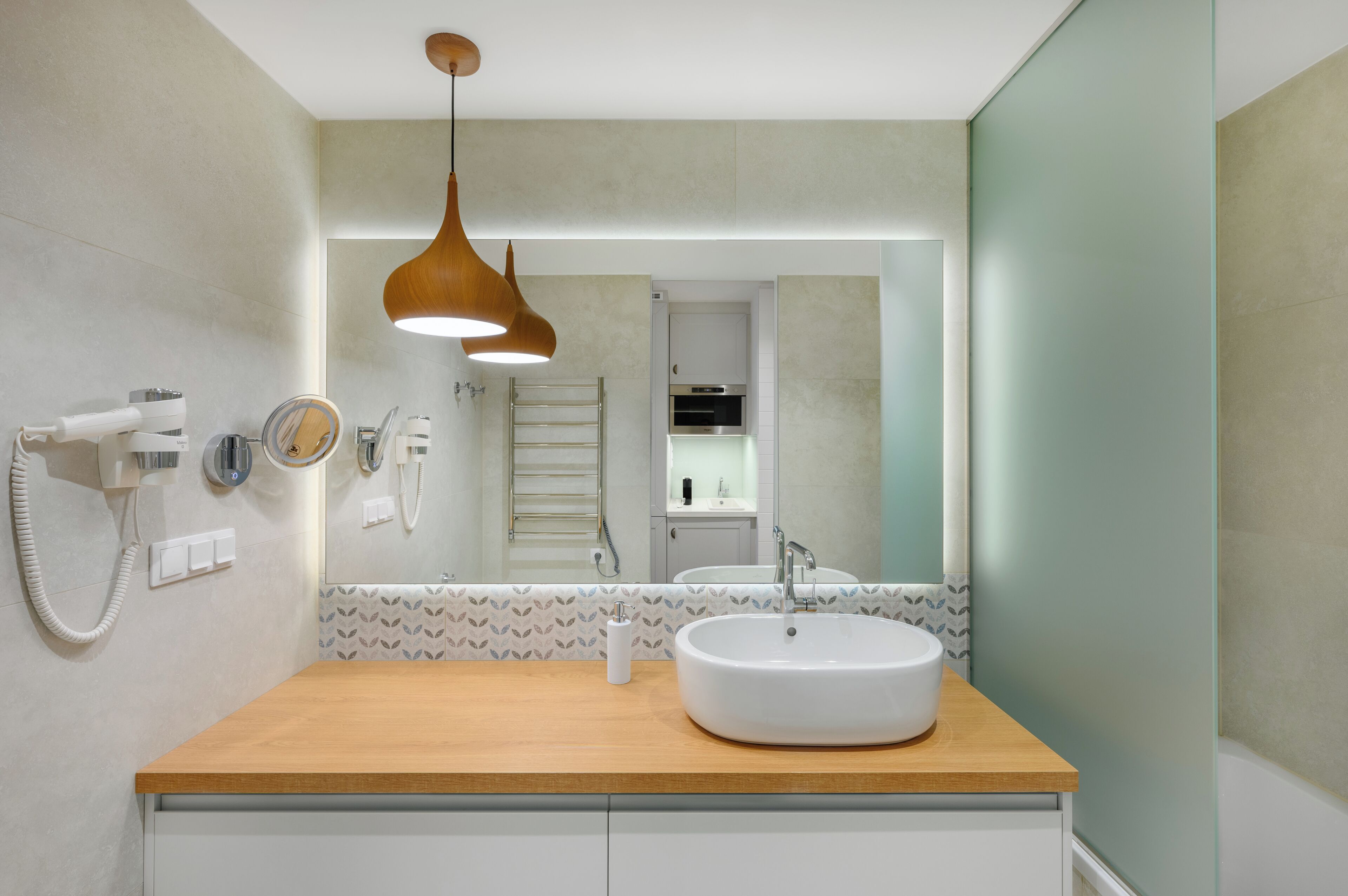 Un baño moderno con tocador de madera, un espejo grande, un lavabo blanco y una lámpara colgante.