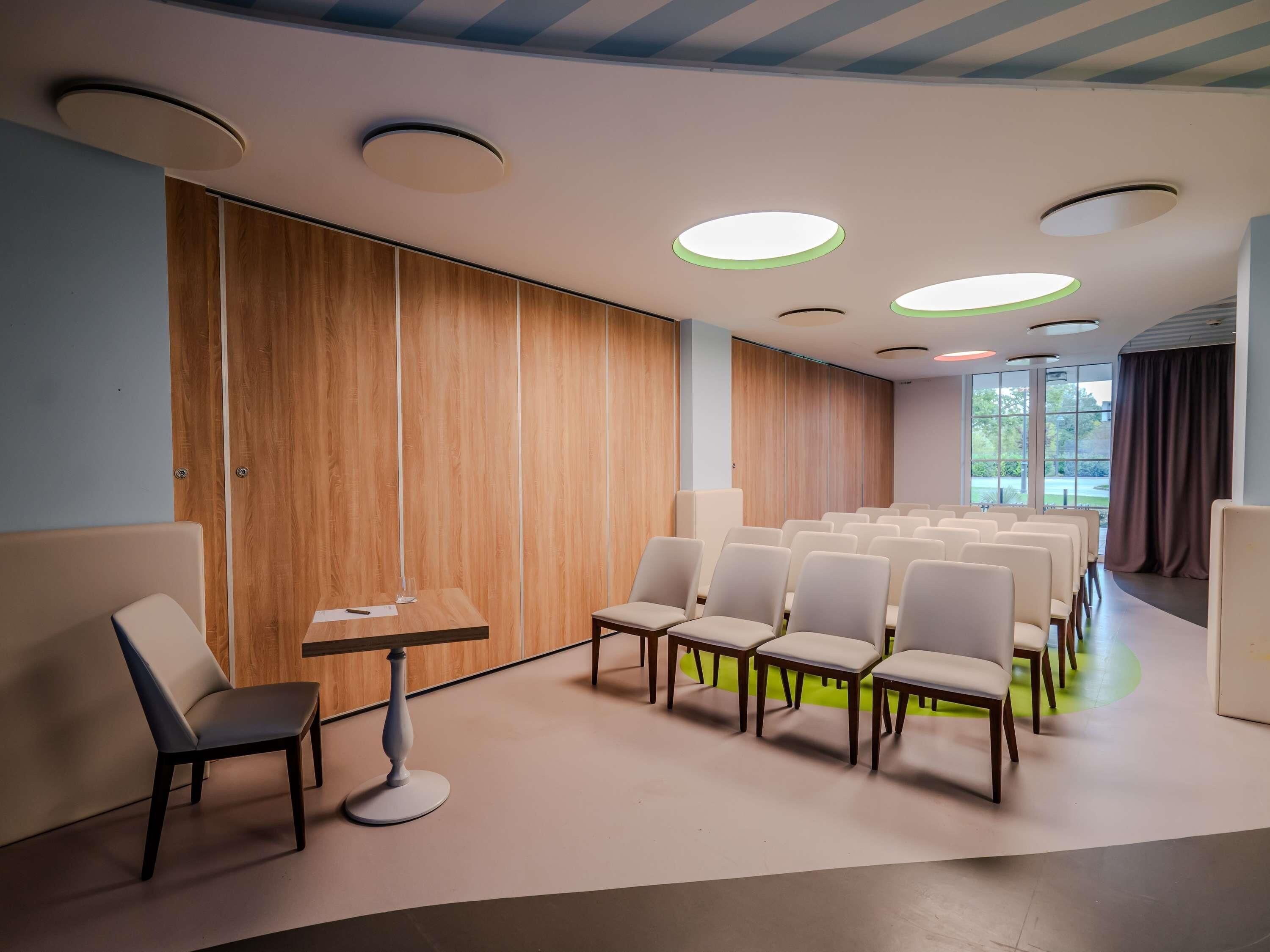 A conference room with rows of chairs, a table with a chair, and a wooden panel wall.