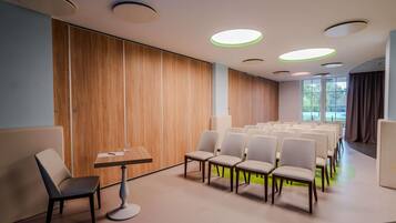 A conference room with rows of chairs, a table with a chair, and a wooden panel wall.