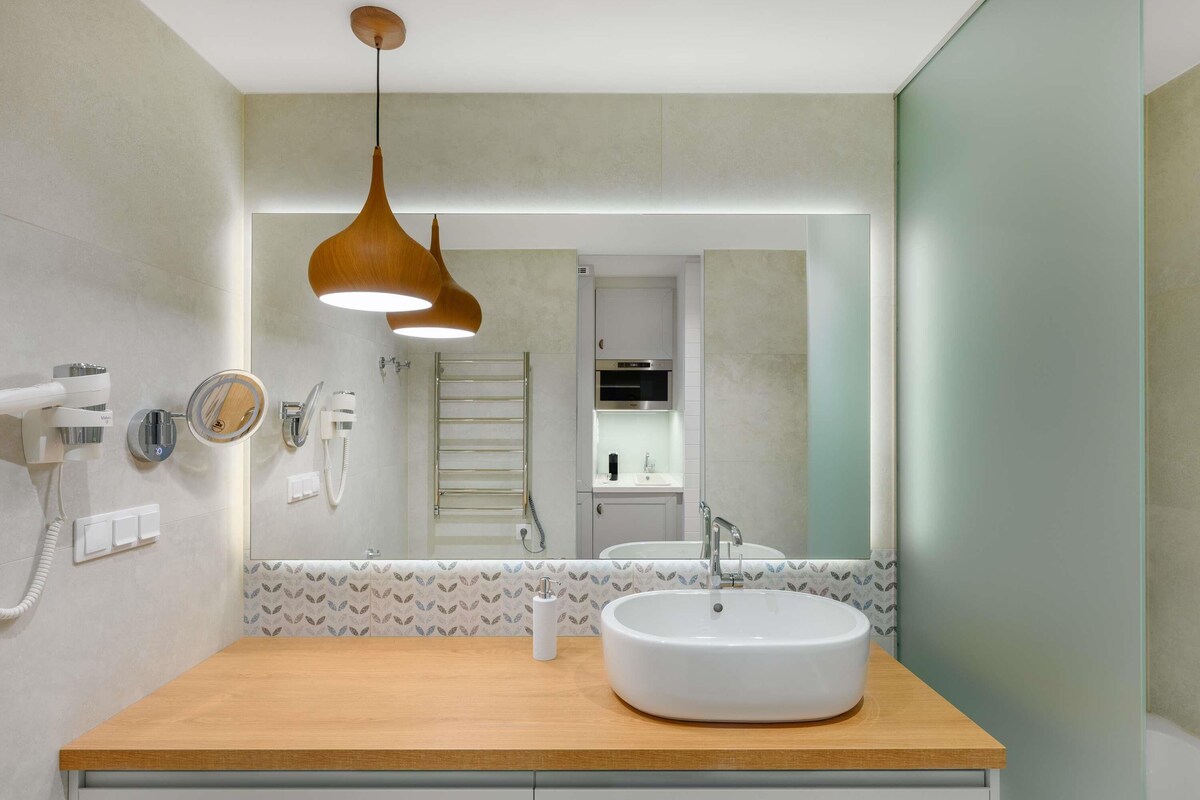 Un baño moderno con tocador de madera, un lavamanos redondo, un perchero para toallas y un espejo.