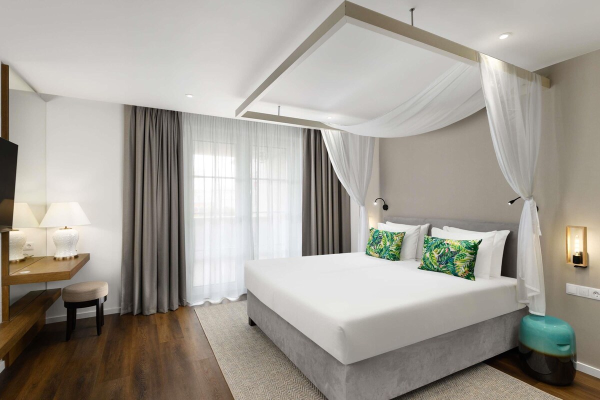 Una habitación de hotel moderna con una cama grande, un escritorio con lámpara y una televisión.