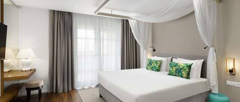 A modern hotel room with a large bed, a desk with a lamp, and a TV.