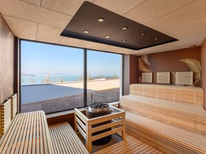 Un espace spa moderne doté d’une grande fenêtre donnant sur la plage, de bancs en bois et d’un espace sauna.