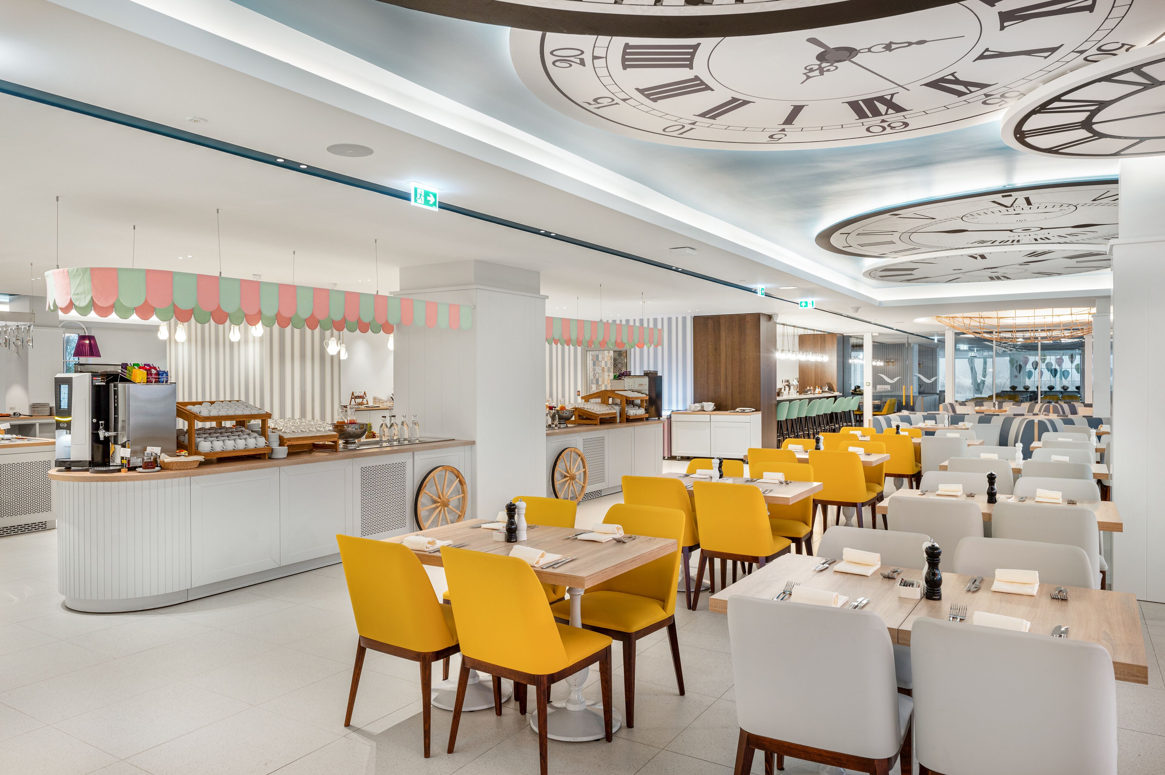 Un restaurante moderno con una isla central, sillas amarillas y un techo con diseños de relojes.