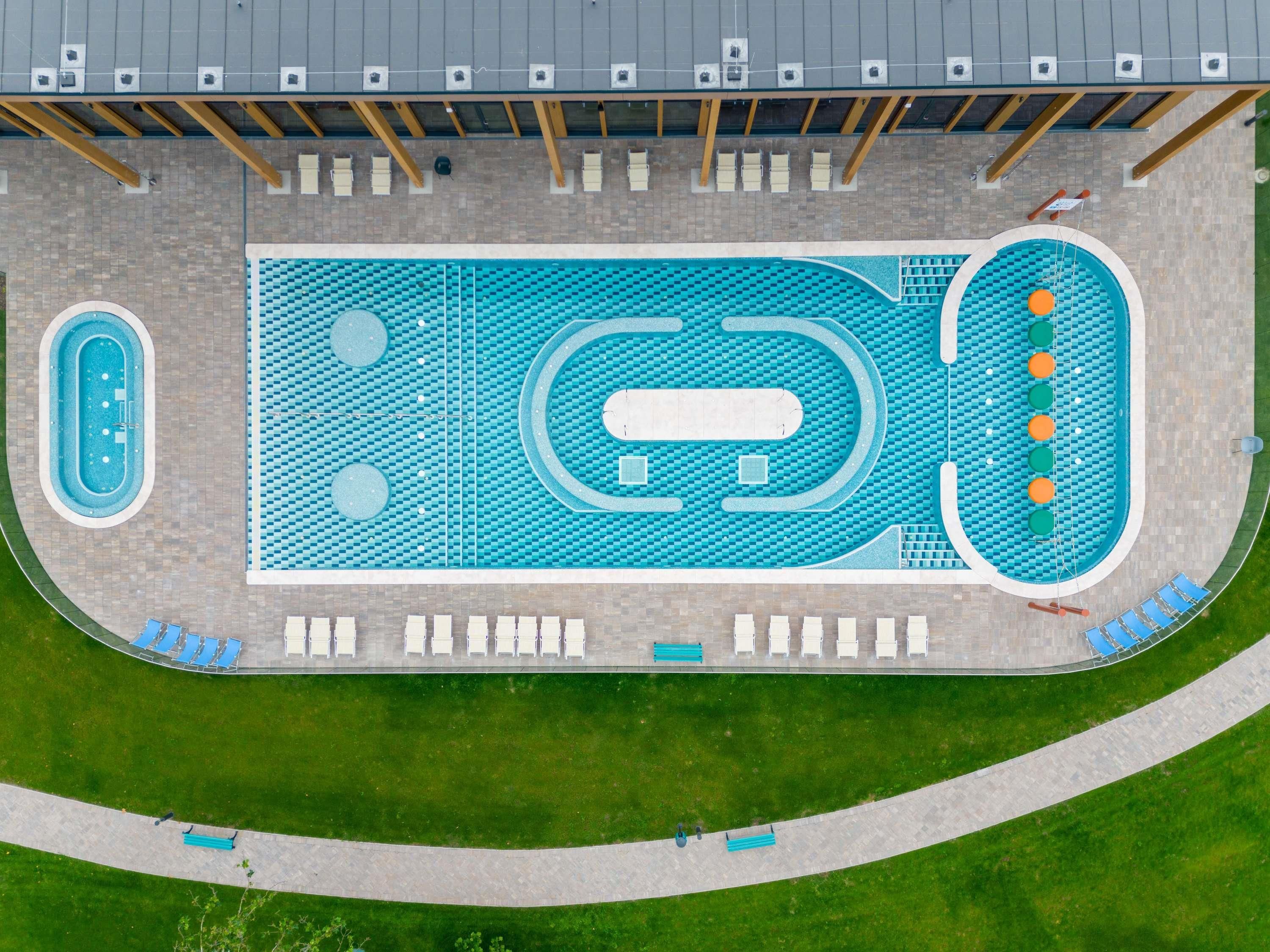 Vista aérea de un complejo de piscinas con varias albercas, sillas de descanso y un paseo que lo rodea.