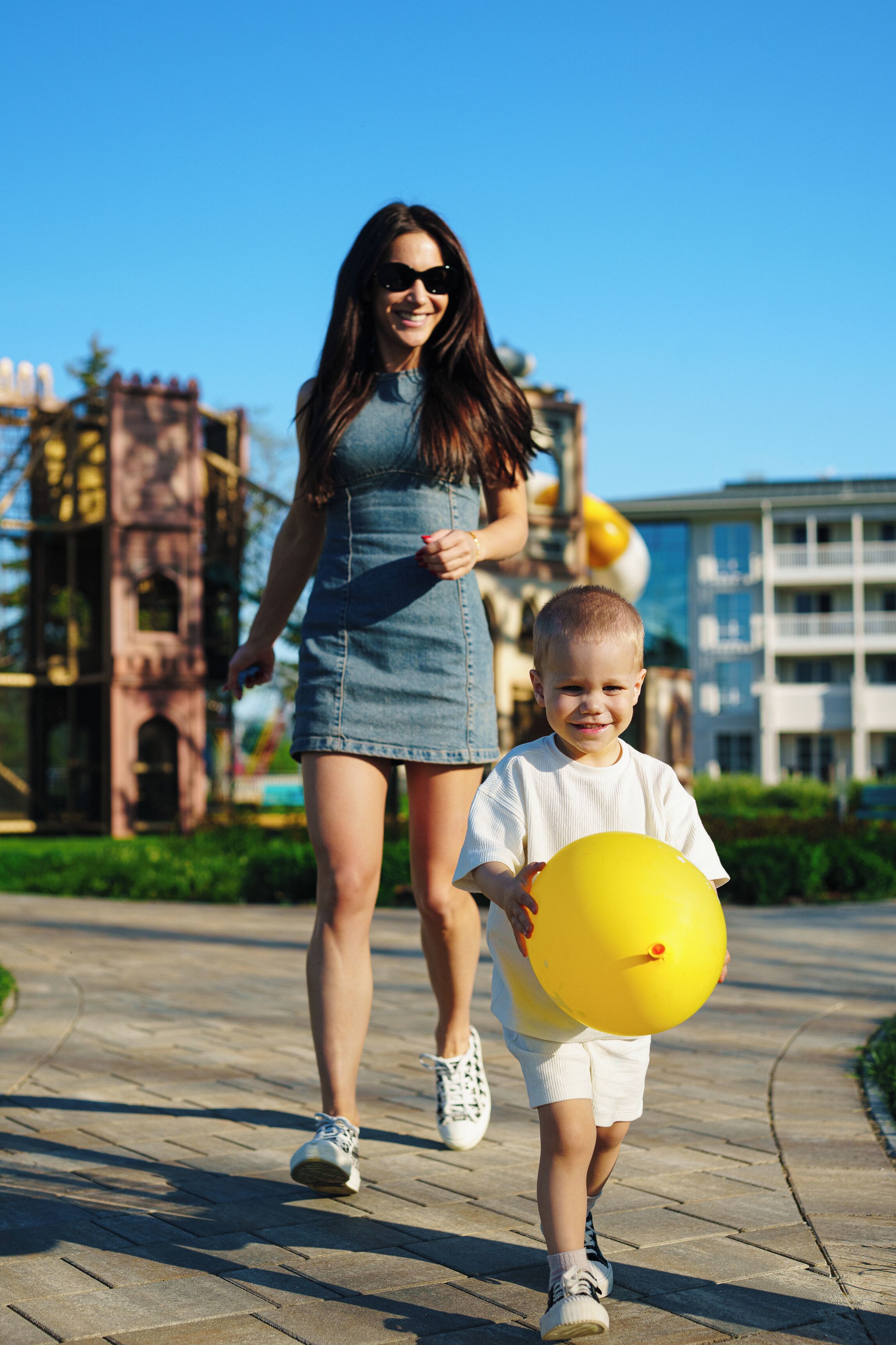 A woman and a child walking on a paved path with a building in the background.