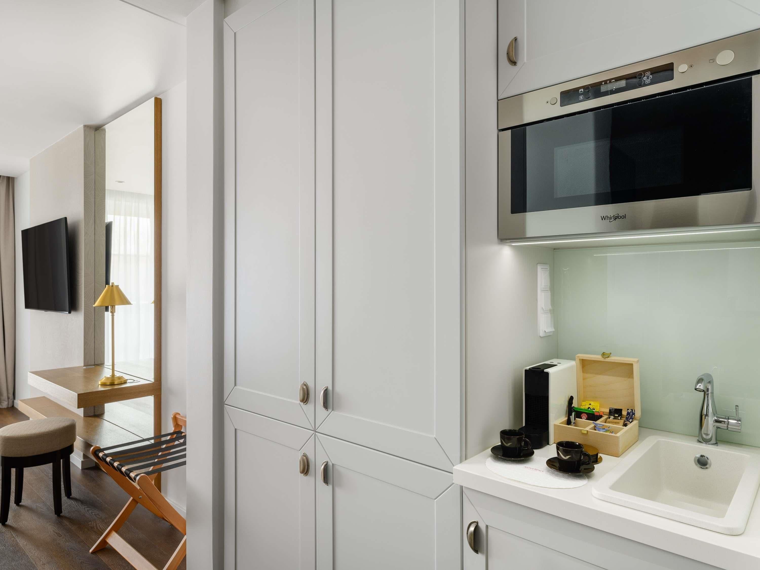 Een moderne hotelkamer met een grote witte kast, een magnetron, een spoelbak, een houten stoel en een televisie.