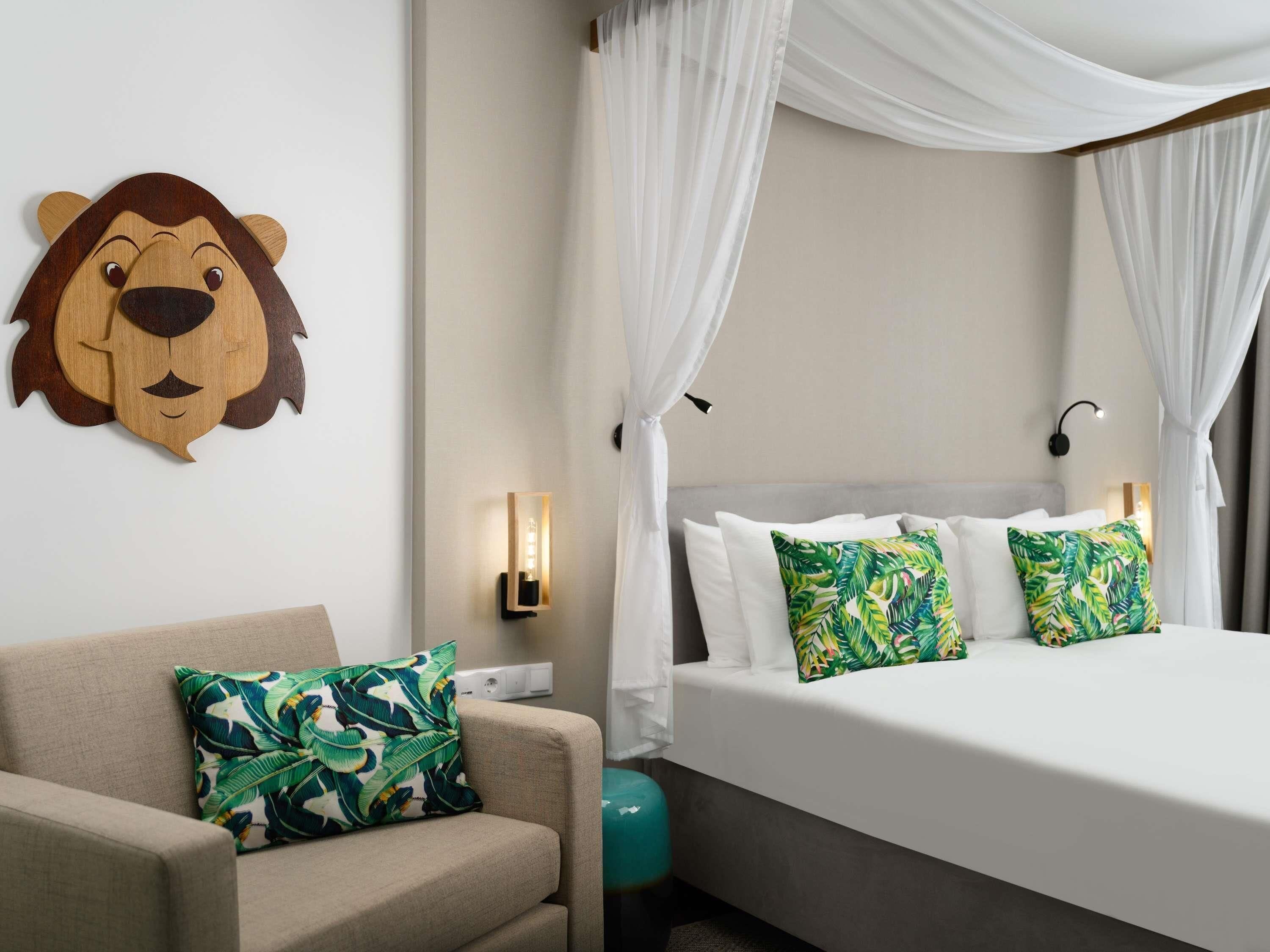 Una habitació d'hotel amb un llit, un sofà, una decoració amb forma de cap de lleó penjada a la paret i una làmpada també penjada a la paret.