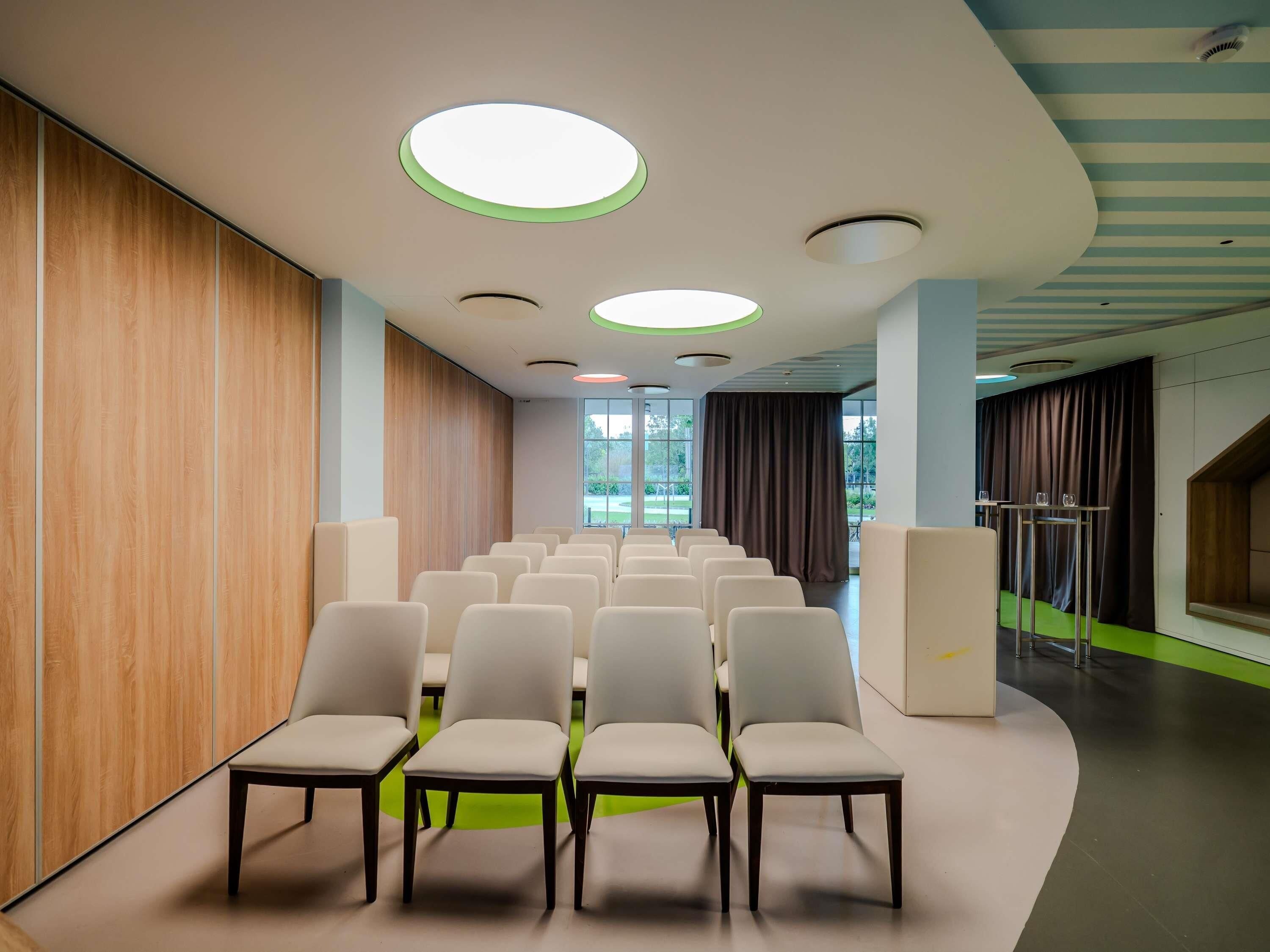 A conference room with rows of chairs, a wooden wall, and a ceiling with circular lights.