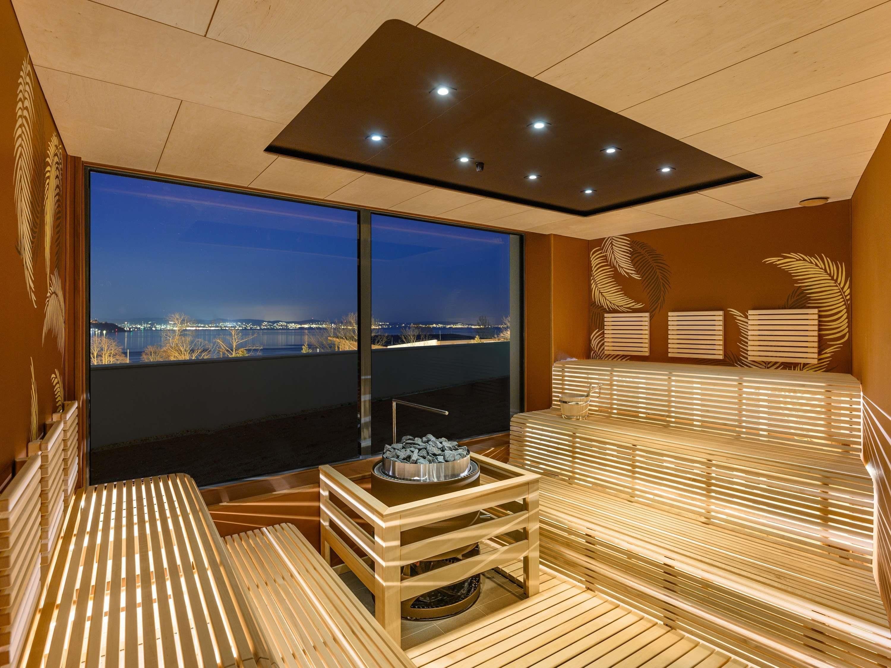 Un cuarto de sauna con un ventanal grande, bancos de madera y un aplique en el techo.