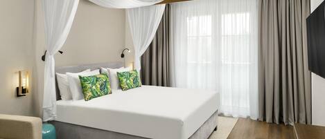 Habitación de hotel moderna con una cama grande, dosel, televisor de pantalla plana y vistas a la ciudad.