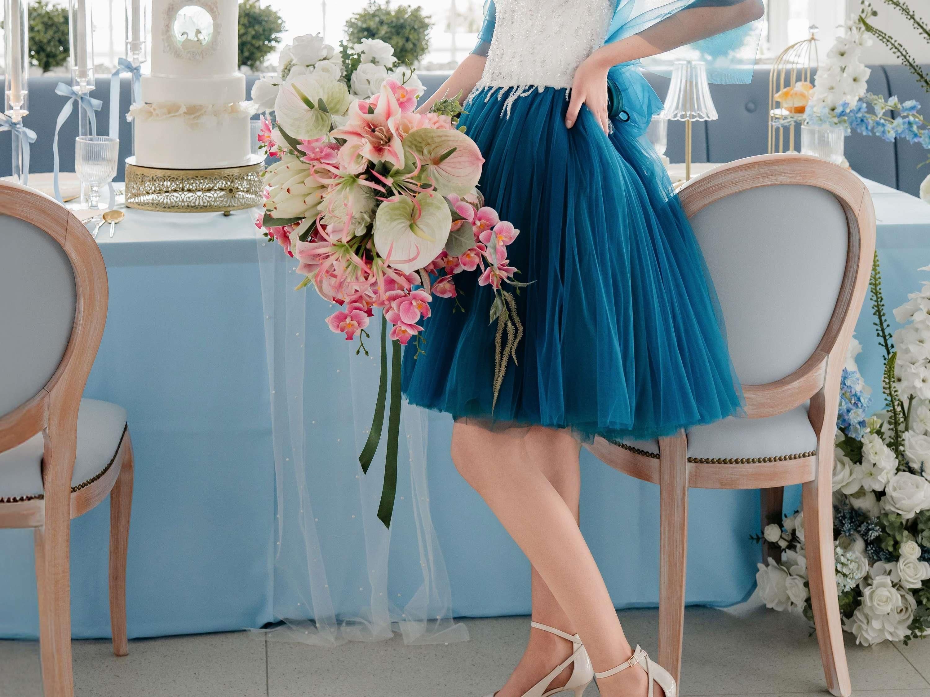 A person seated at a table with a cake and floral arrangement.