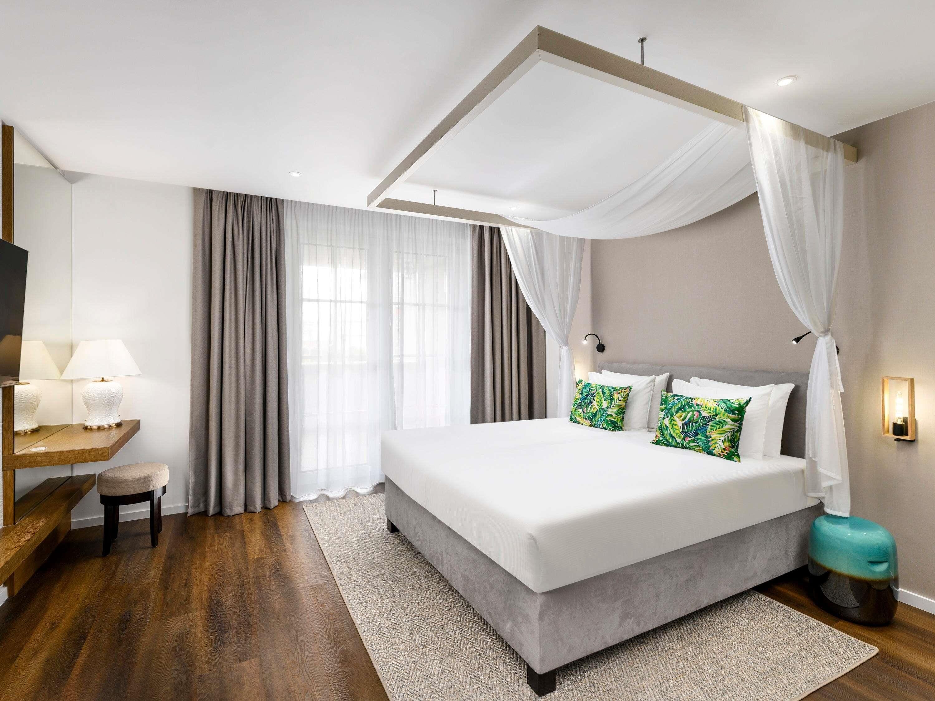 Habitació d'hotel moderna amb un llit gran, un escriptori amb una làmpada i una televisió.