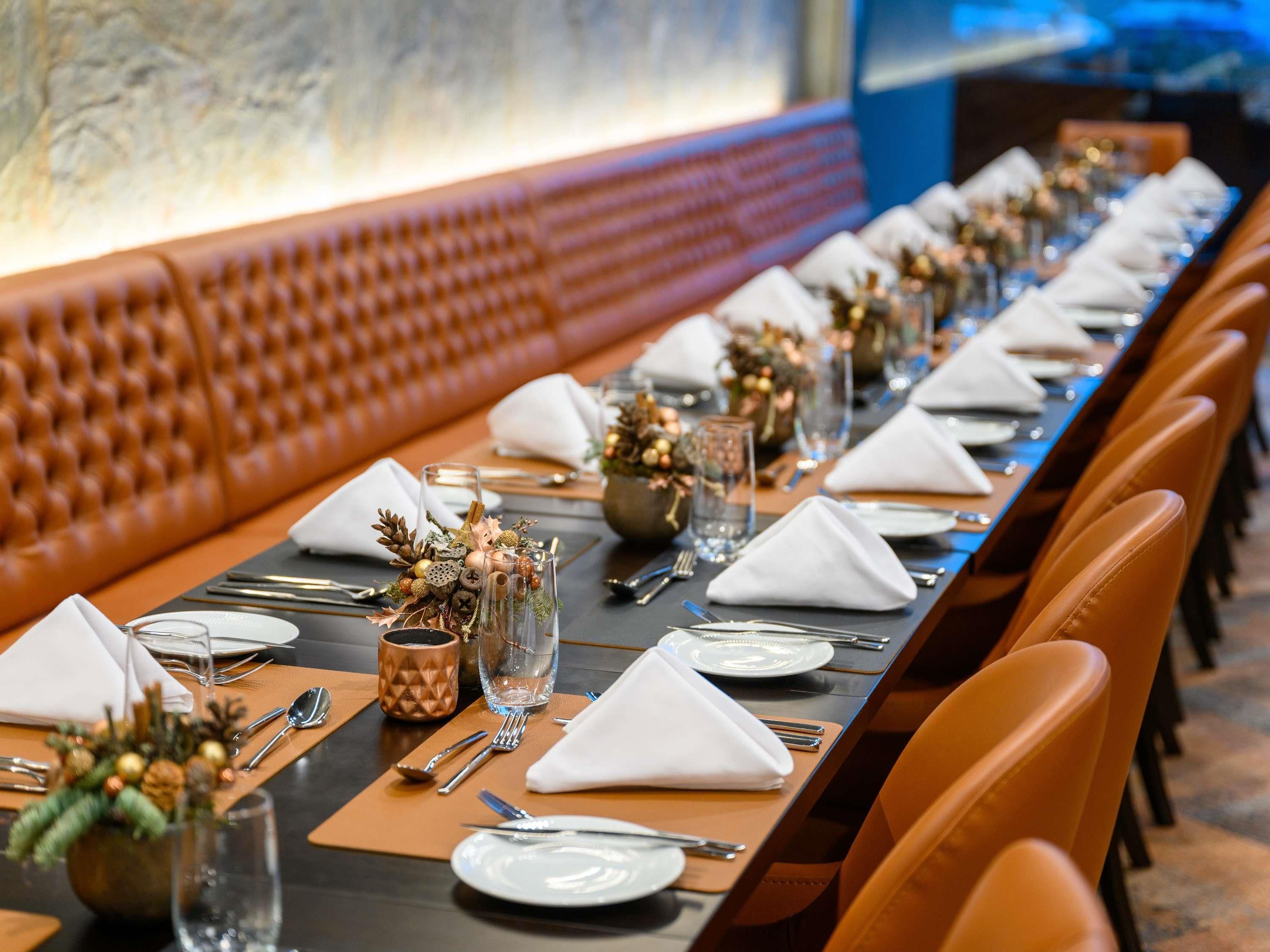 Una larga mesa de comedor dispuesta con servilletas blancas, platos y cubiertos, flanqueada por sillas de cuero.