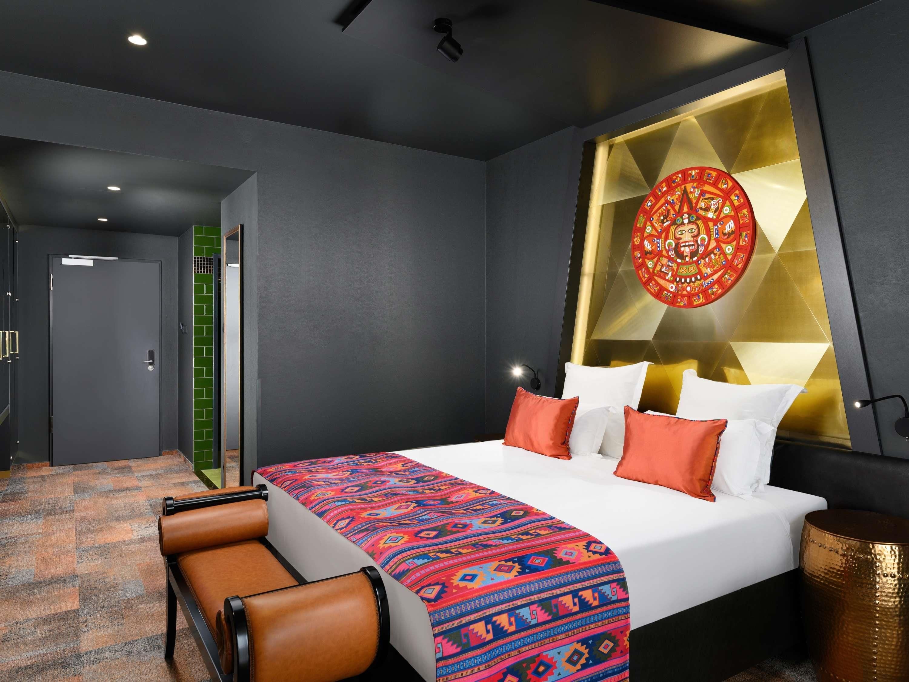 A modern hotel room with a large bed, a patterned throw blanket, and a decorative wall piece.