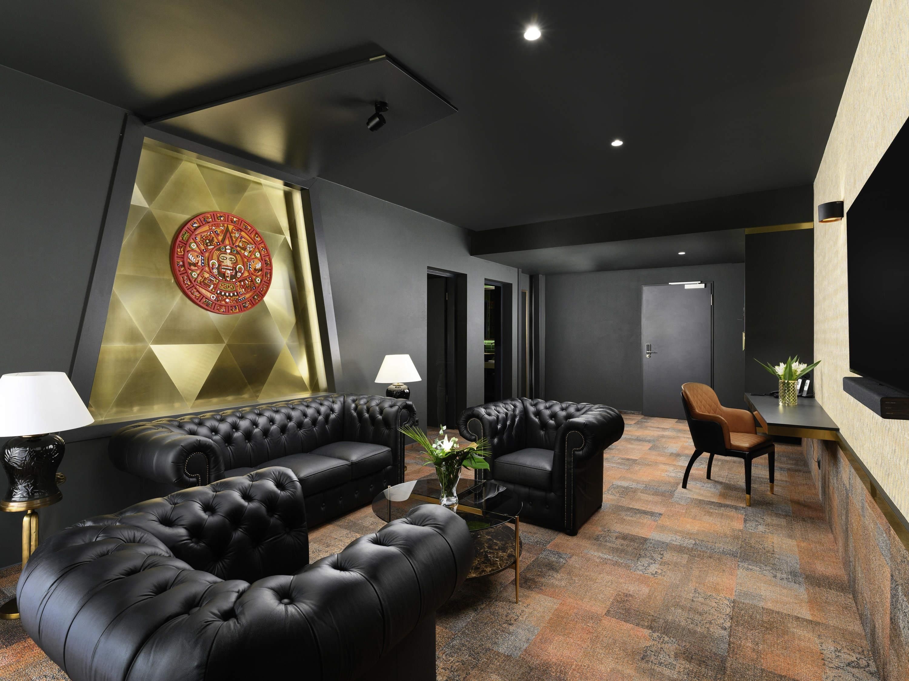 Un área de descanso moderna con un sofá de cuero negro, una mesa de centro y un elemento decorativo en la pared.