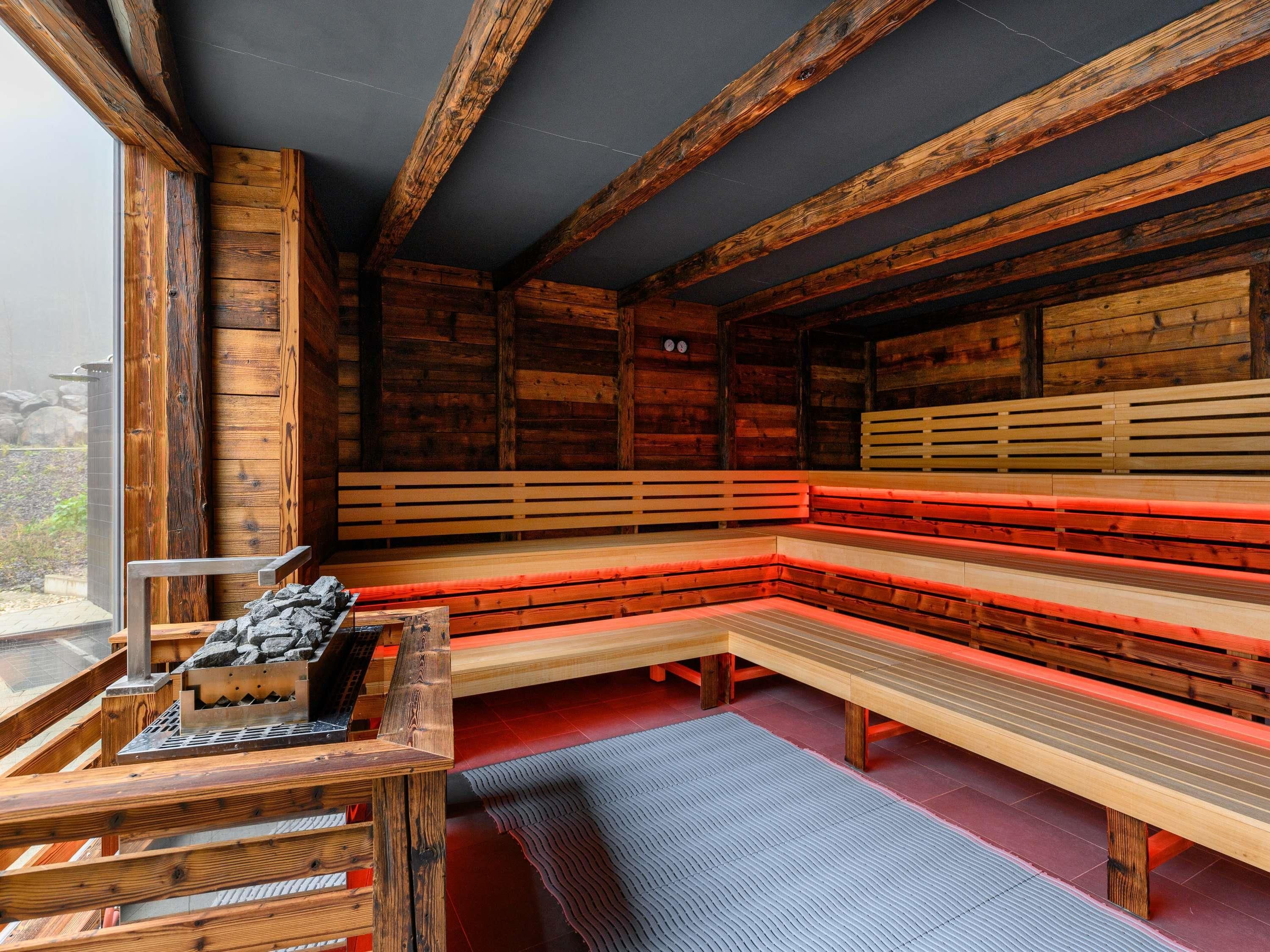 A sauna with wooden benches, a stone bench, and a sauna table with stones.