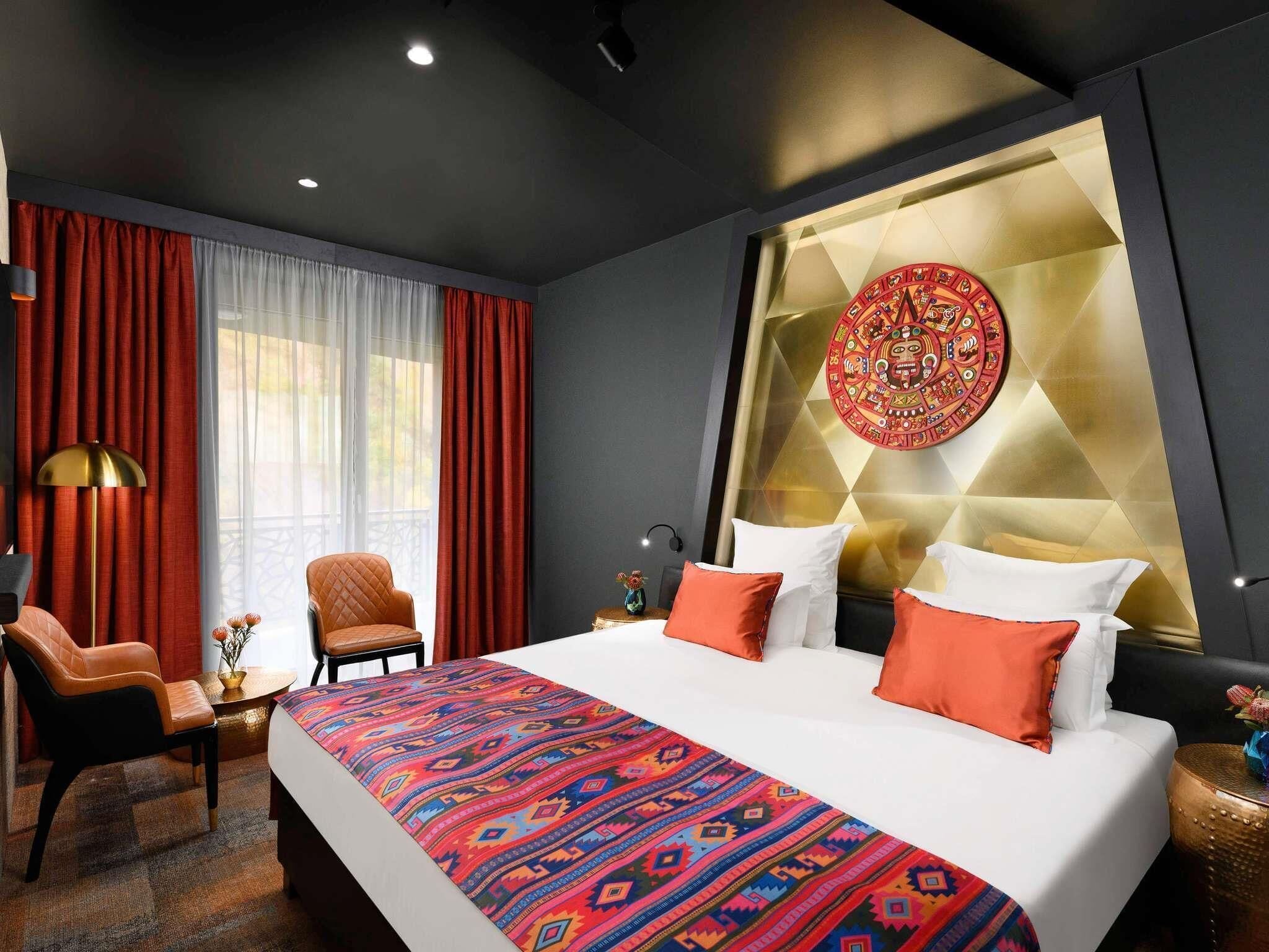 A hotel room with a bed, a chair, a desk, and a wall with a decorative emblem.