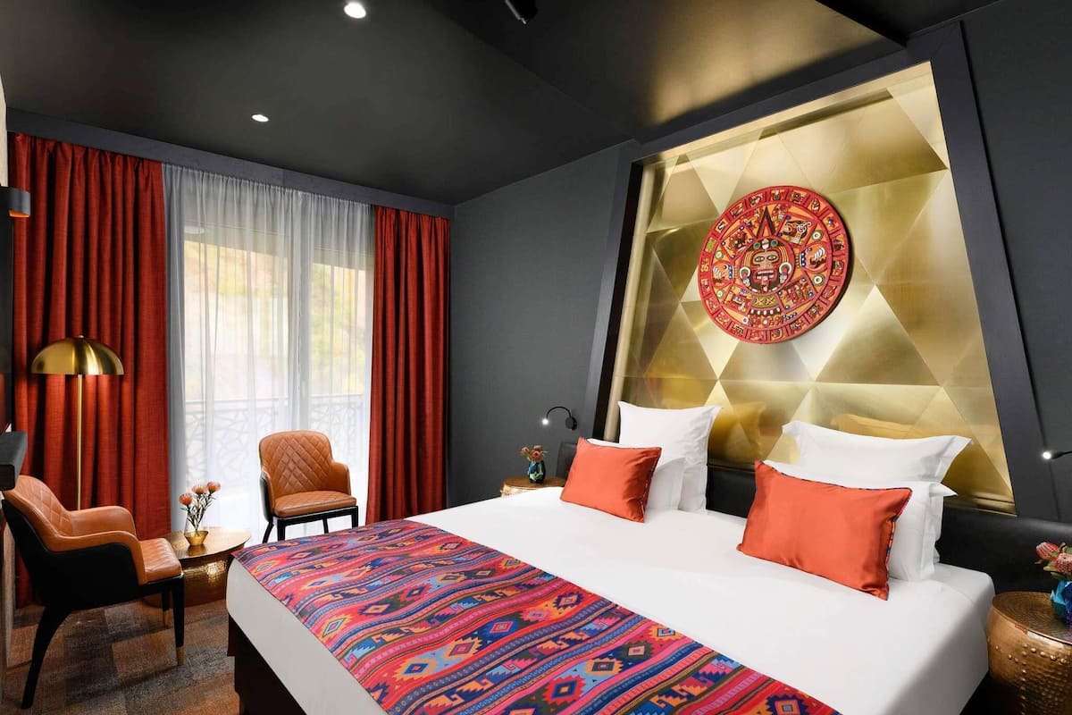 Une chambre dâhĂŽtel comprenant un lit, une chaise, un bureau et un mur ornĂ© dâun motif dĂ©coratif.