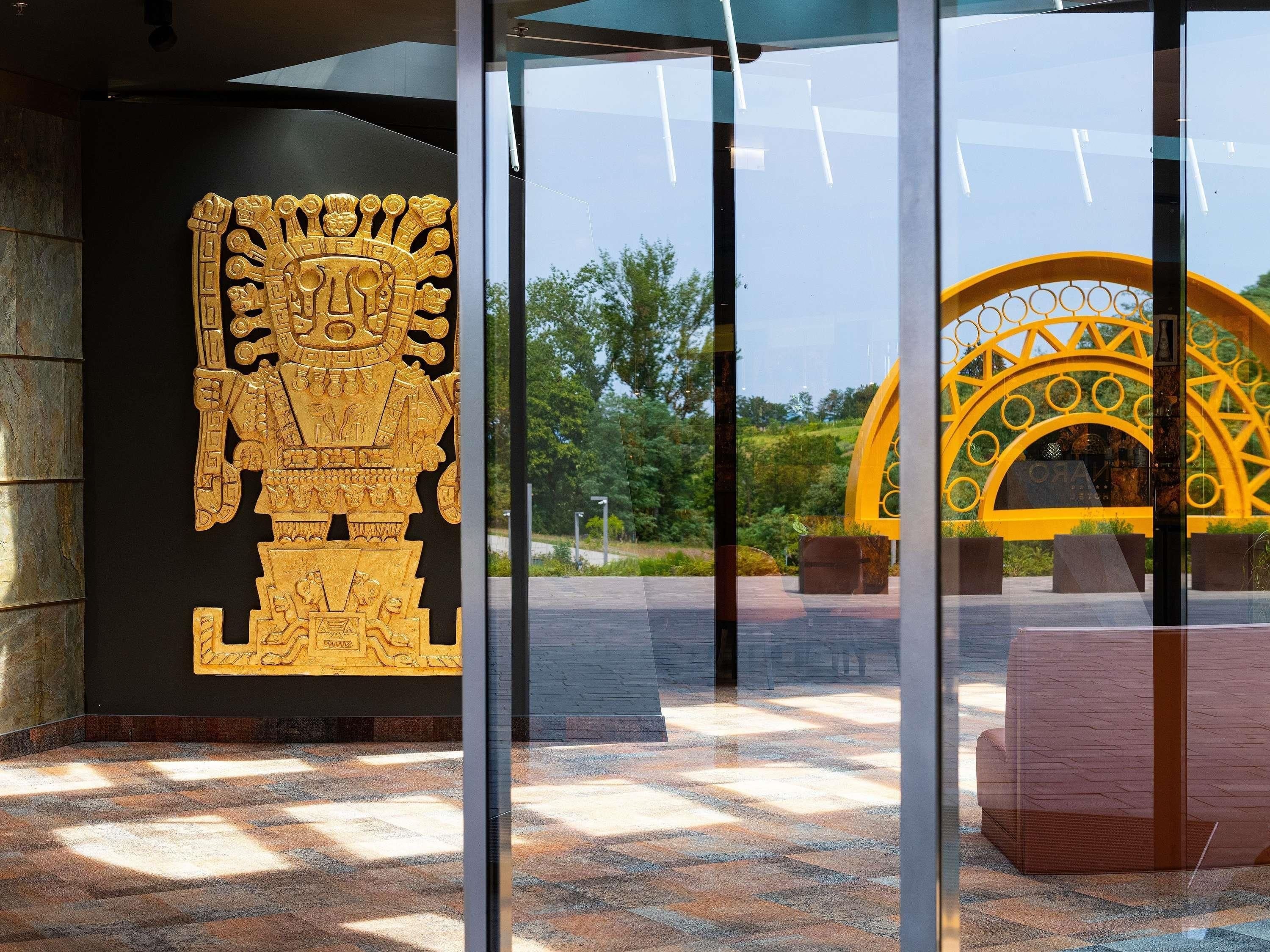 Una entrada de edificio moderno con una gran escultura dorada y un arco amarillo.