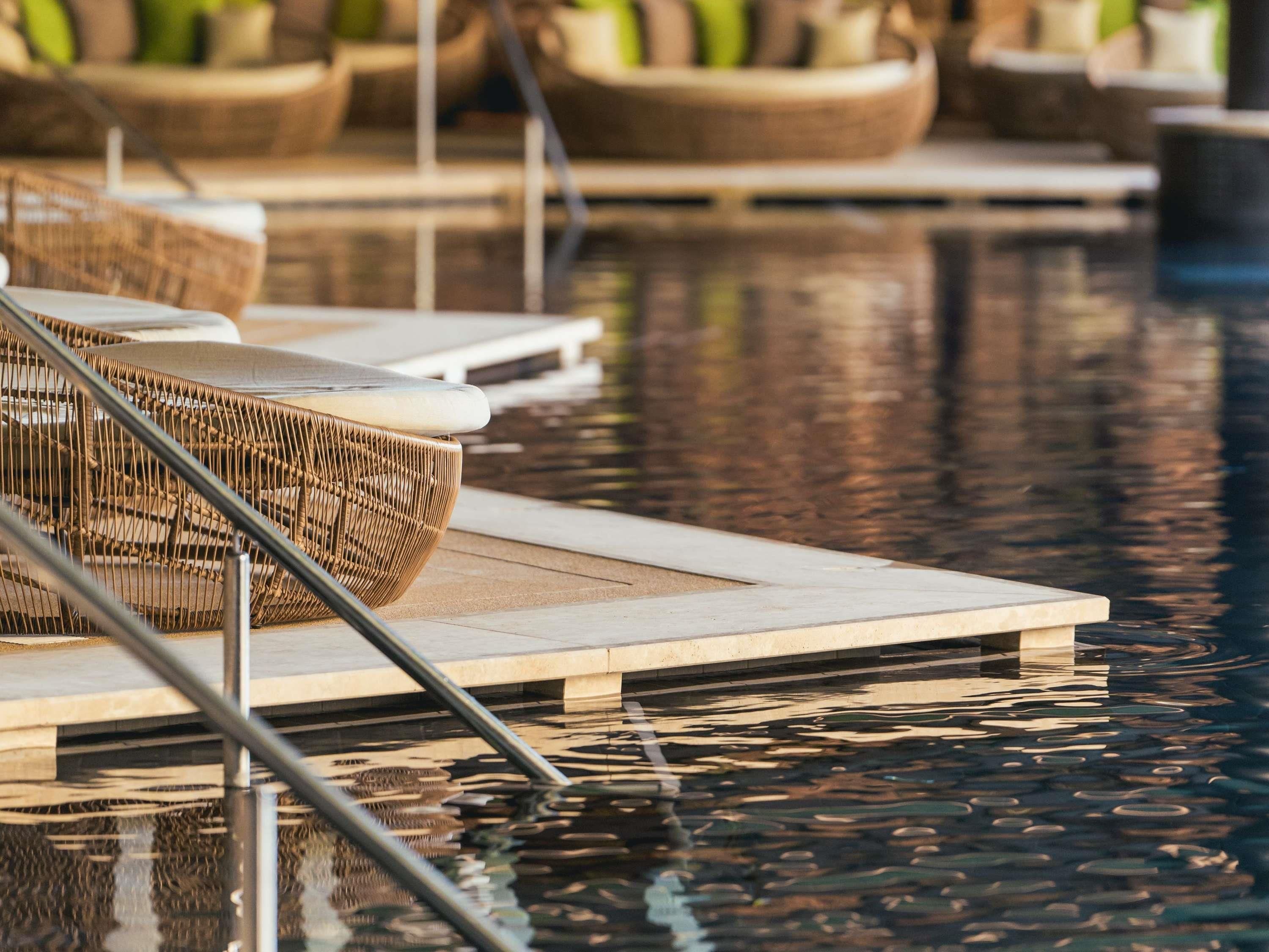 Zona junto a la piscina con sillones de mimbre y vista despejada al agua.