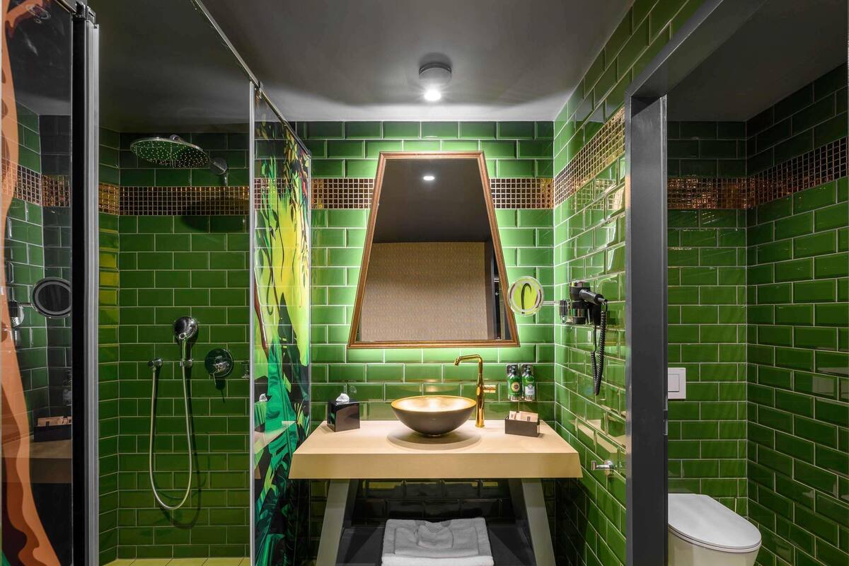 A bathroom with green tiles, a sink, a mirror, a shower, and a toilet.
