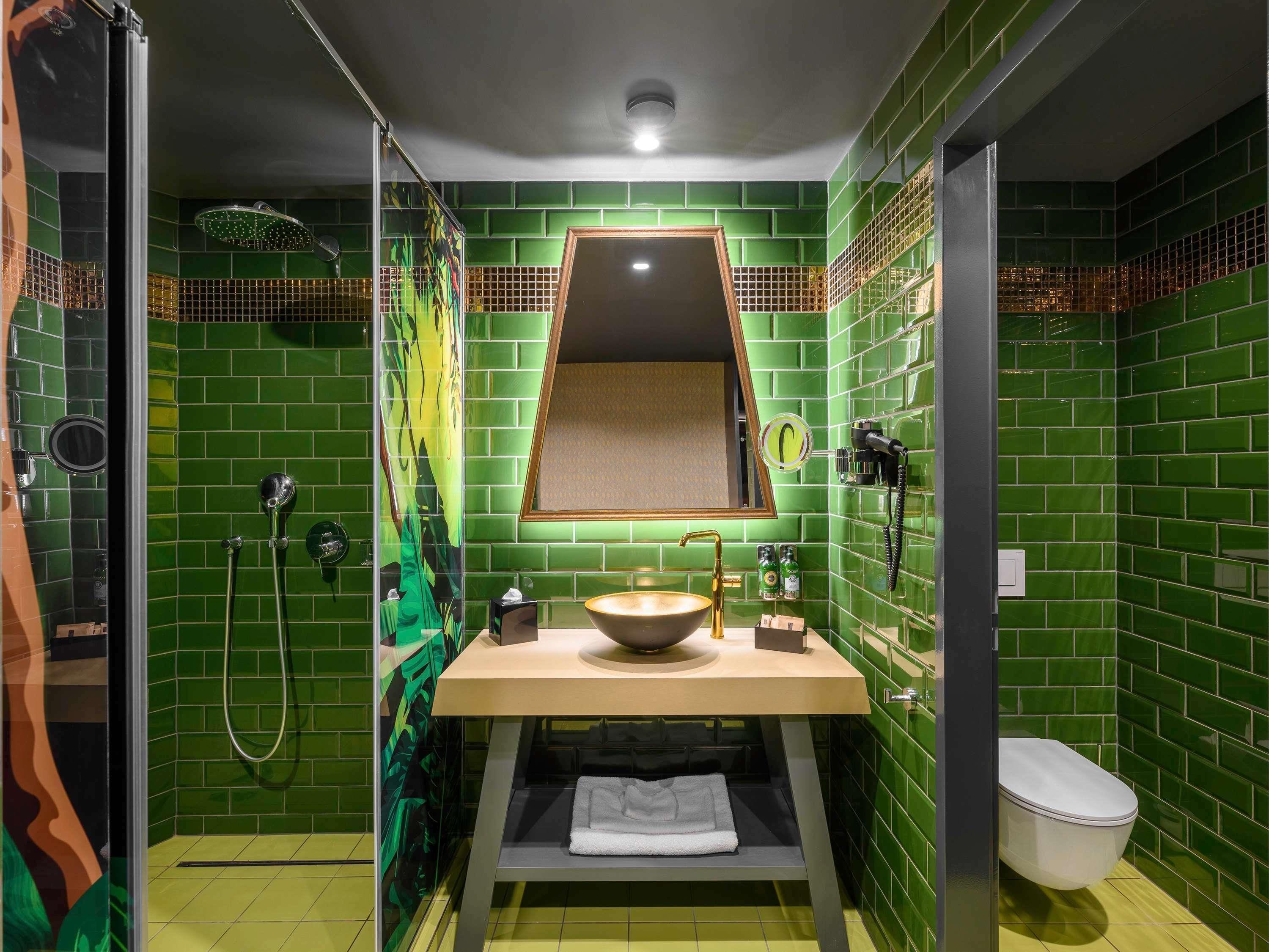 A bathroom with green tiles, a sink, a mirror, a shower, and a toilet.