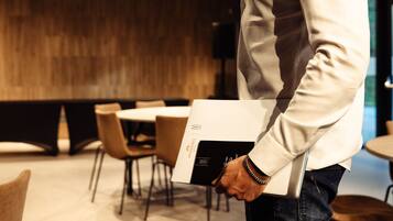 A person holding a book with a logo, standing in a room with tables and chairs.