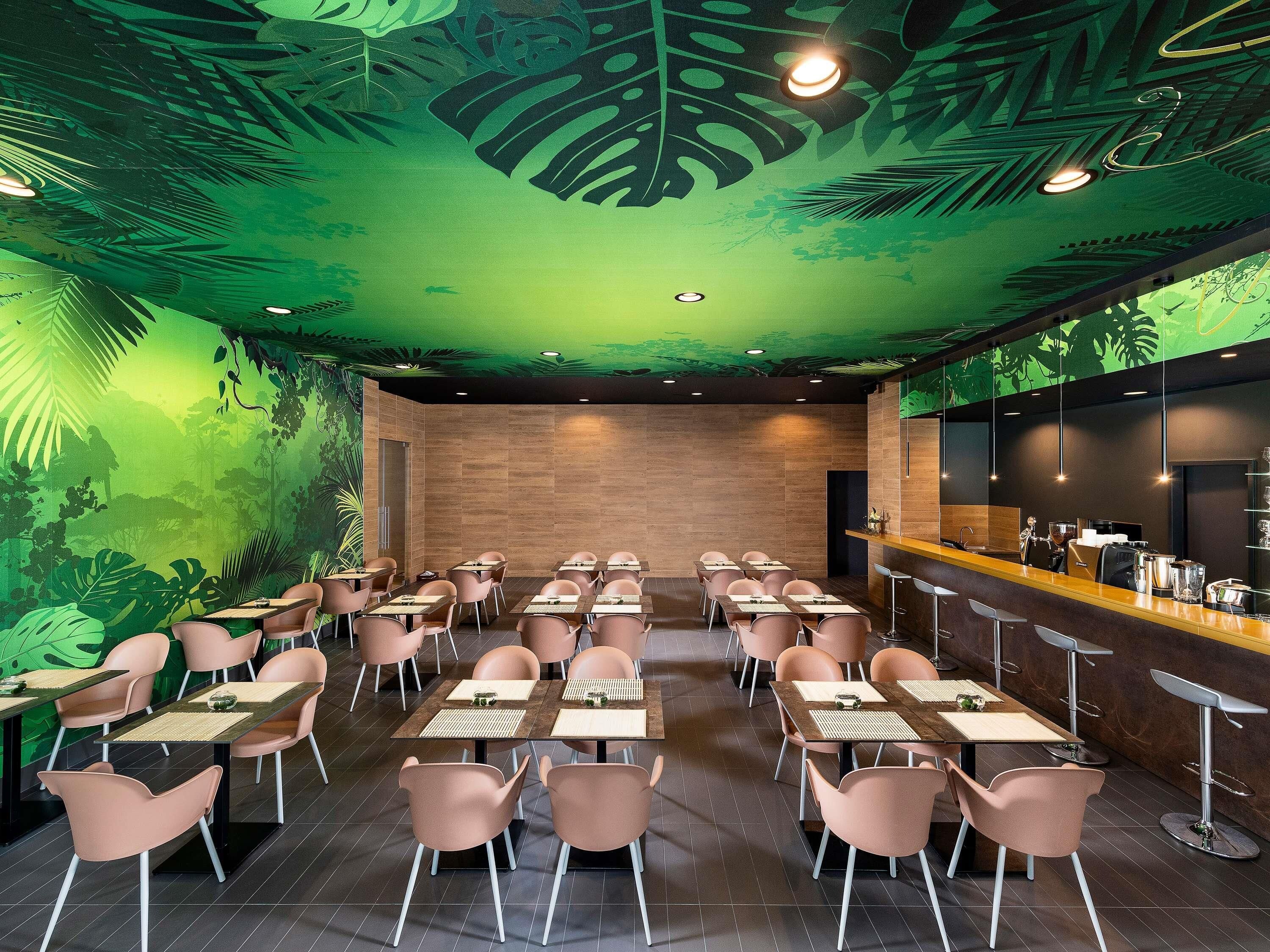 A restaurant with a green leaf-themed ceiling, multiple tables with chairs, and a bar area.