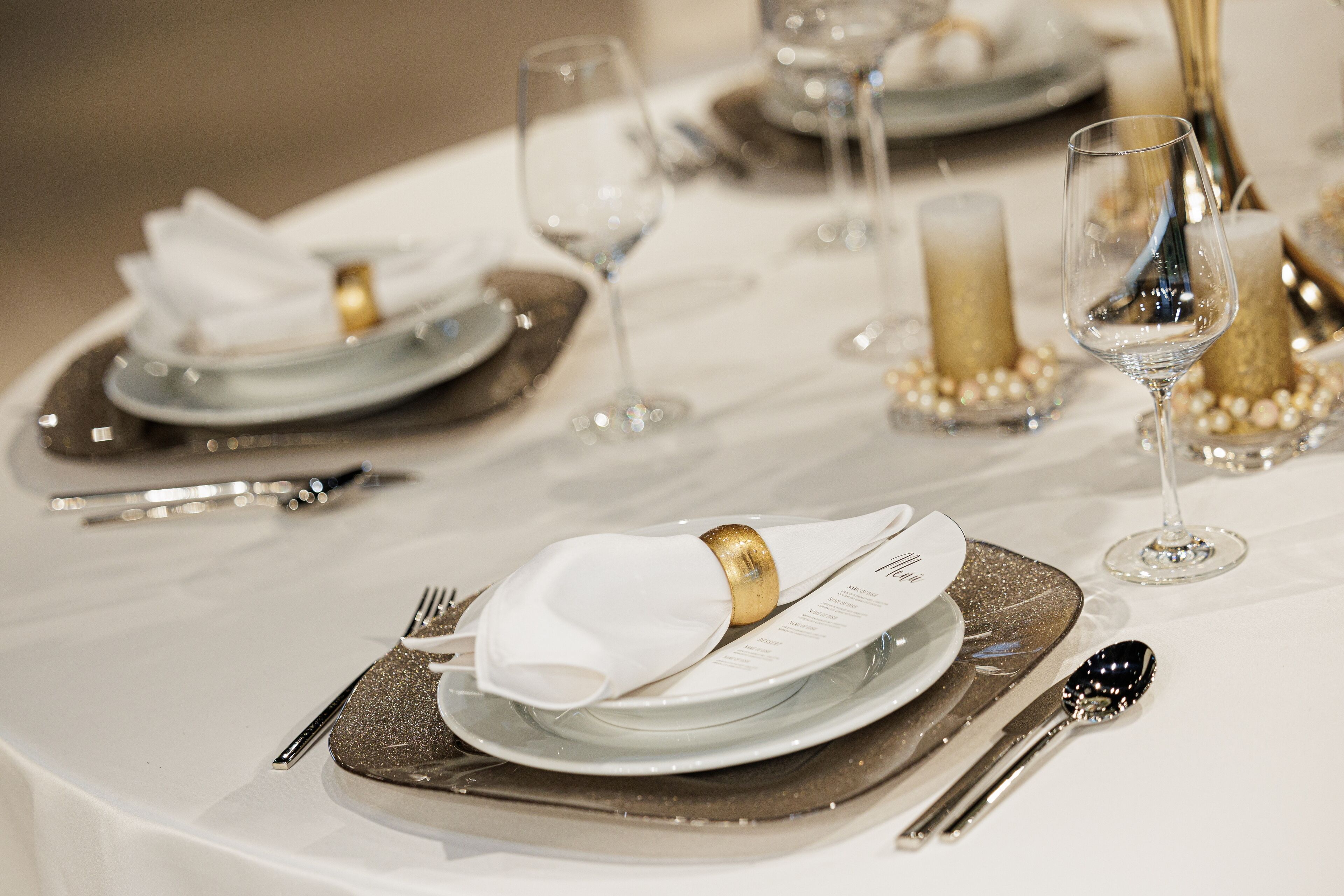 A table set for a formal event with white plates, gold accents, and clear glassware.