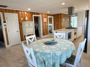 A dining area with a round table, white chairs, and a kitchen in the background.
