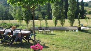 Un espace extérieur verdoyant avec une table et des chaises, un banc en bois et un pot de fleurs.