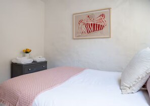 Ein Schlafzimmer mit einem Bett, einem Nachttisch mit Handtüchern, einem gerahmten Kunstwerk an der Wand und einer Vase mit Blumen.