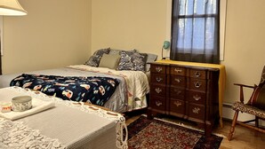 Een slaapkamer met een bed, een dressoir, een stoel, een raam en een lamp.