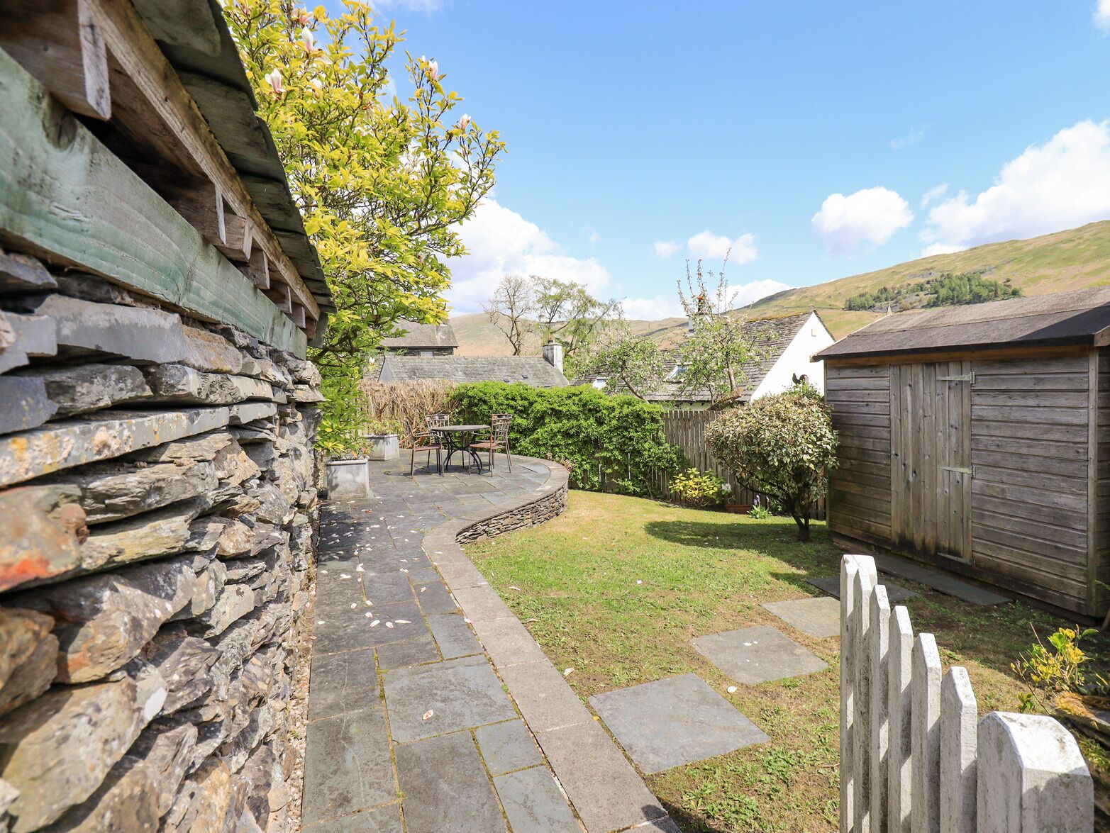 A stone wall, a wooden fence, a grassy yard, and a white building with a sloped roof.