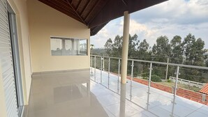 A spacious balcony with a tiled floor, a wooden ceiling, and a view of trees and hills. - Spacious and cozy country house to welcome your family. (Alumínio)