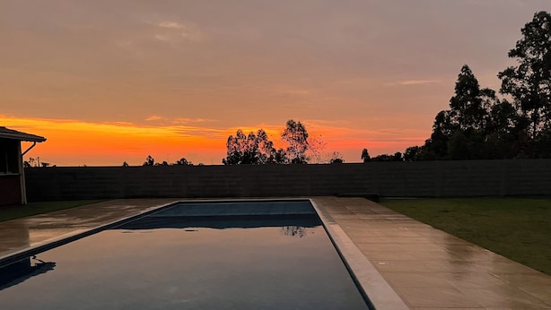 A rectangular swimming pool with a tiled border, surrounded by a low stone wall, and a grassy area with trees in the background. - Spacious and cozy country house to welcome your family. (Alumínio)