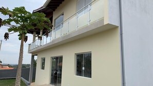 A two-story building with a balcony, large windows, and a small garden area. - Spacious and cozy country house to welcome your family. (Alumínio)