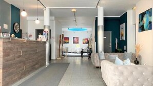 Un hall d’hôtel moderne avec un comptoir d’accueil, un espace salon et des œuvres d’art accrochées aux murs.