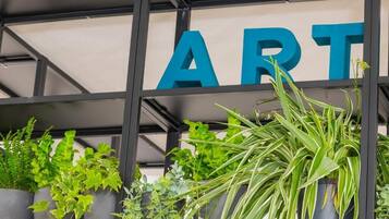 Una pared con la palabra "ART" en letras azules grandes, rodeada de plantas en macetas.