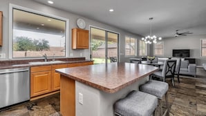 A modern kitchen with a large island, wooden cabinets, and a dining area with a gray sofa and chairs. - Spacious 5 BR, 3.5 BA, 4000+sf, WiFi, Pool,Hot Tub (Gilbert)