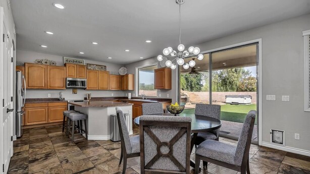 A modern kitchen with wooden cabinets, a central island, and a dining area with grey upholstered chairs. - Spacious 5 BR, 3.5 BA, 4000+sf, WiFi, Pool,Hot Tub (Gilbert)