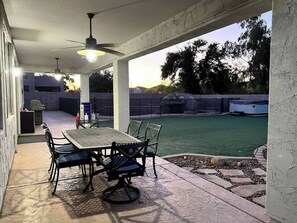An outdoor patio with a table and chairs, a ceiling fan, and a view of a backyard with a pool and trees. - Spacious 5 BR, 3.5 BA, 4000+sf, WiFi, Pool,Hot Tub (Gilbert)