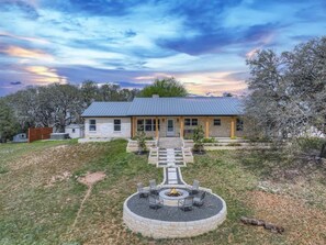 A two-story house with a stone exterior, a front porch, and a circular fire pit in the yard. - Starlight Meadows Hot-tub 3mi to Downtown (Fredericksburg)
