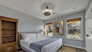 Une chambre à coucher avec un lit, une armoire en bois, deux fenêtres et un ventilateur de plafond.