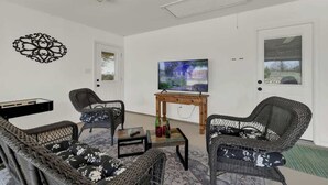 A furnished living room with wicker furniture, a flat-screen TV, and a door with a window. - Starlight Meadows Hot-tub 3mi to Downtown (Fredericksburg)